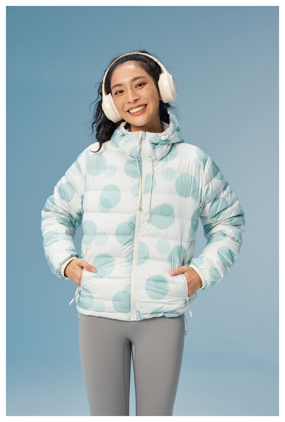 Model wearing a white hooded puffer jacket with pale aqua circles, front view with the zipper and pockets visible.