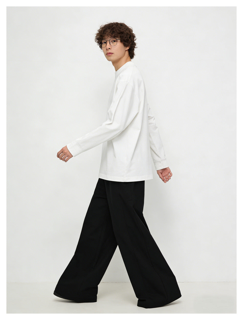 Model walking in a loose white long-sleeve crewneck shirt, shown from the side with black wide-leg trousers.