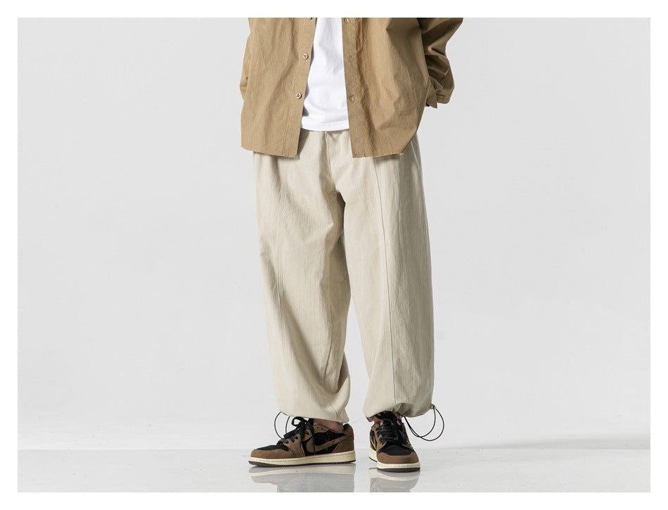 Front view of a model wearing loose light beige trousers with adjustable drawcord hems.