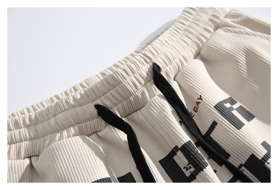Close-up of the gathered waistband, black drawstrings, and partial print on ivory shorts.