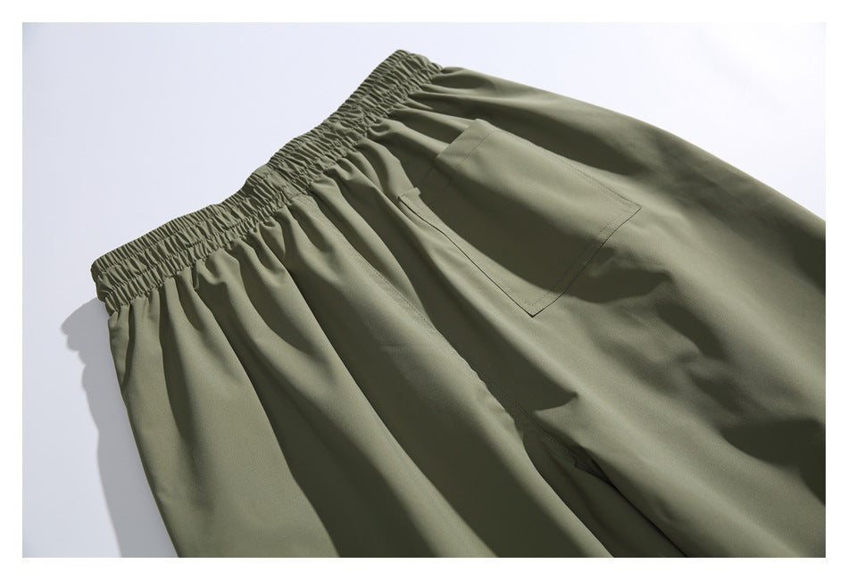 Olive-green pants laid flat, with a gathered elastic waistband and a patch pocket.