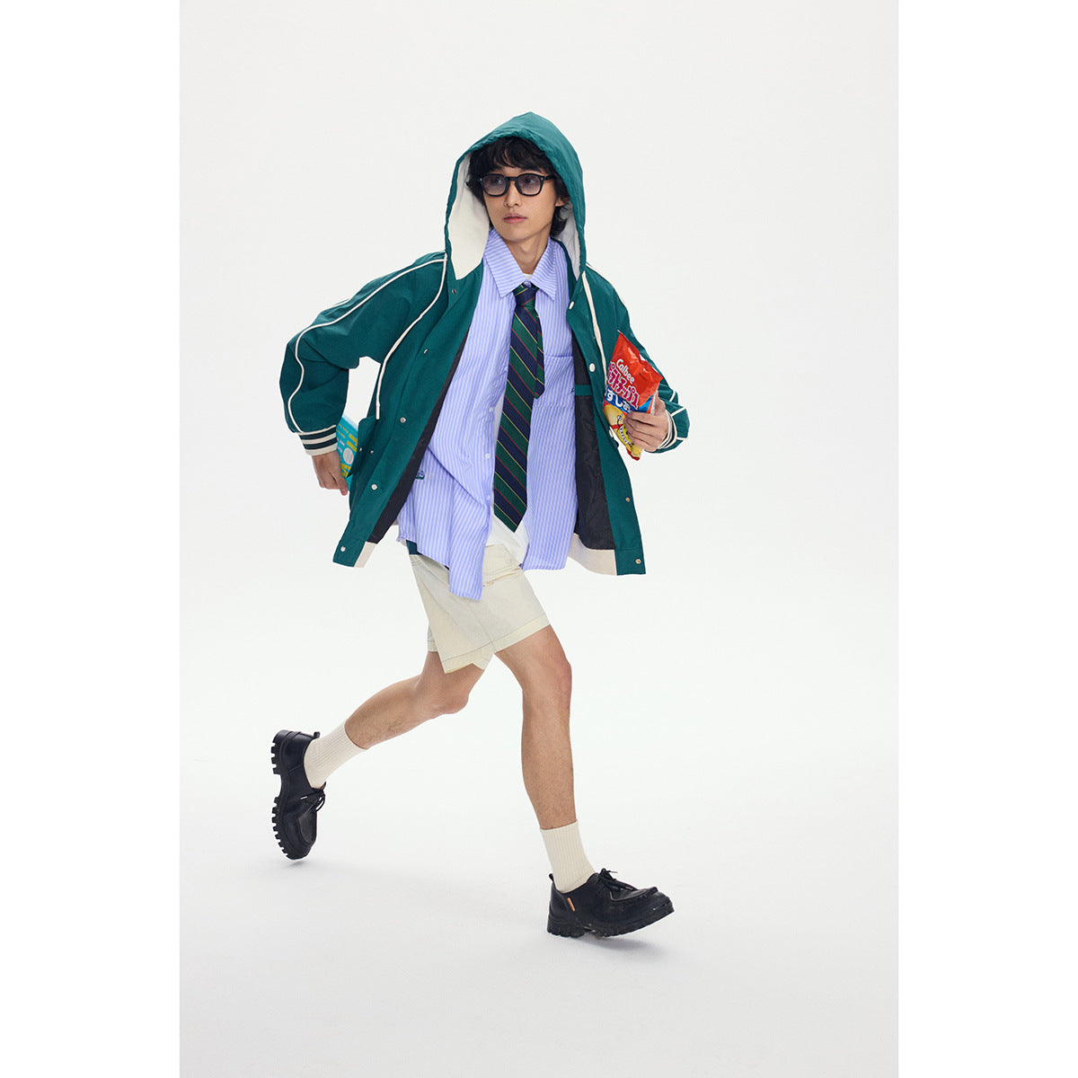 Model wearing an open teal hooded jacket with cream piping and striped cuffs over a blue shirt and tie.