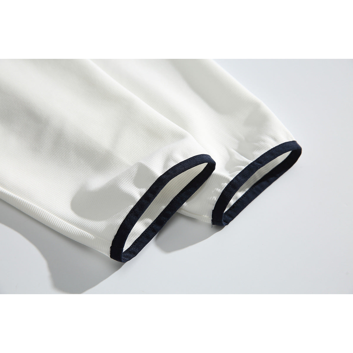 Close-up of two off-white sleeve cuffs finished with dark navy trim.