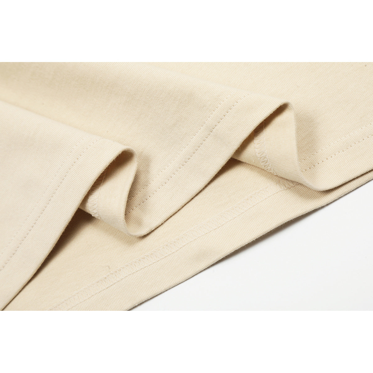 Close-up of the cream T-shirt's folded hem and stitching.