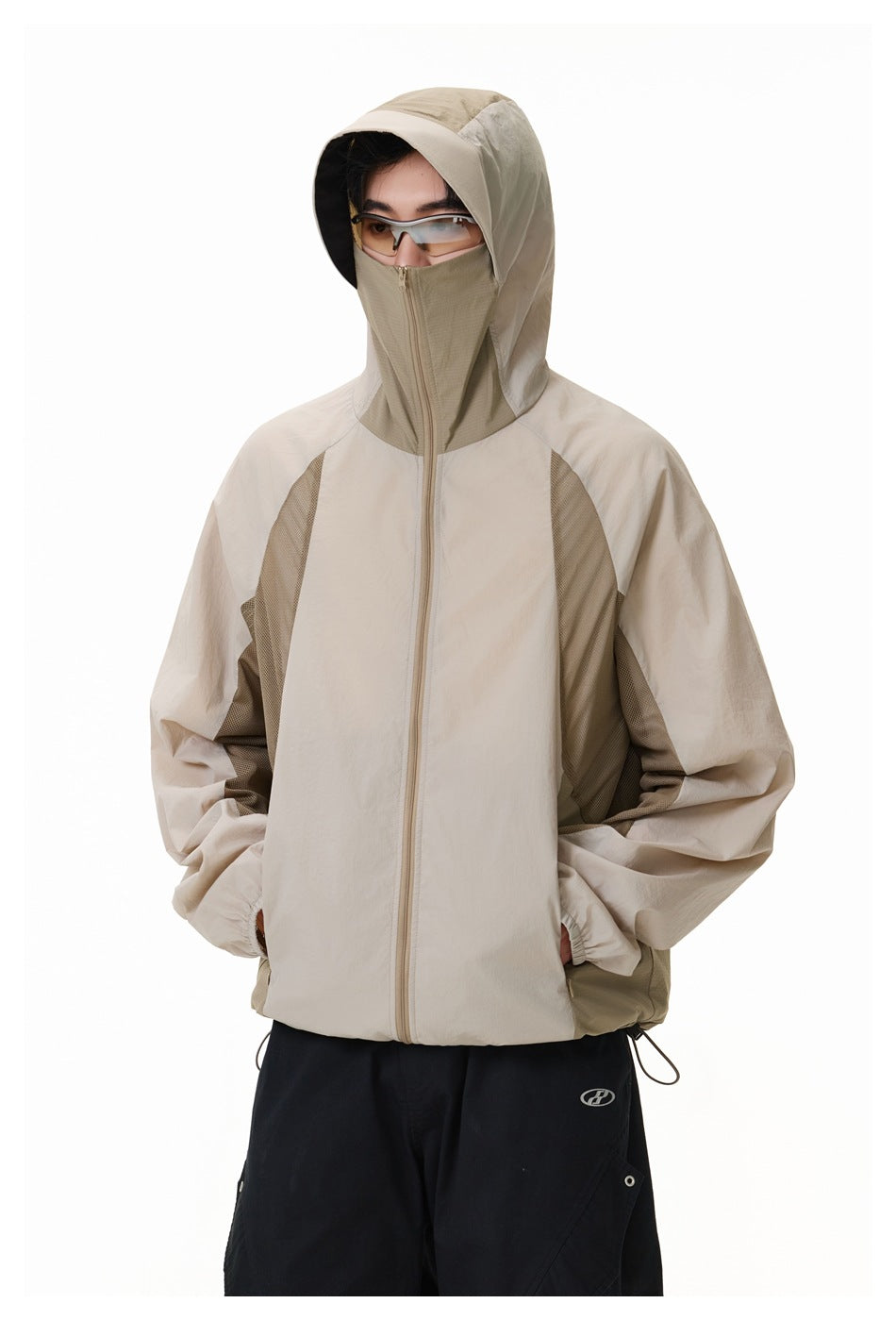 Model wearing a light beige hooded jacket zipped over the face, with contrasting mesh panels.