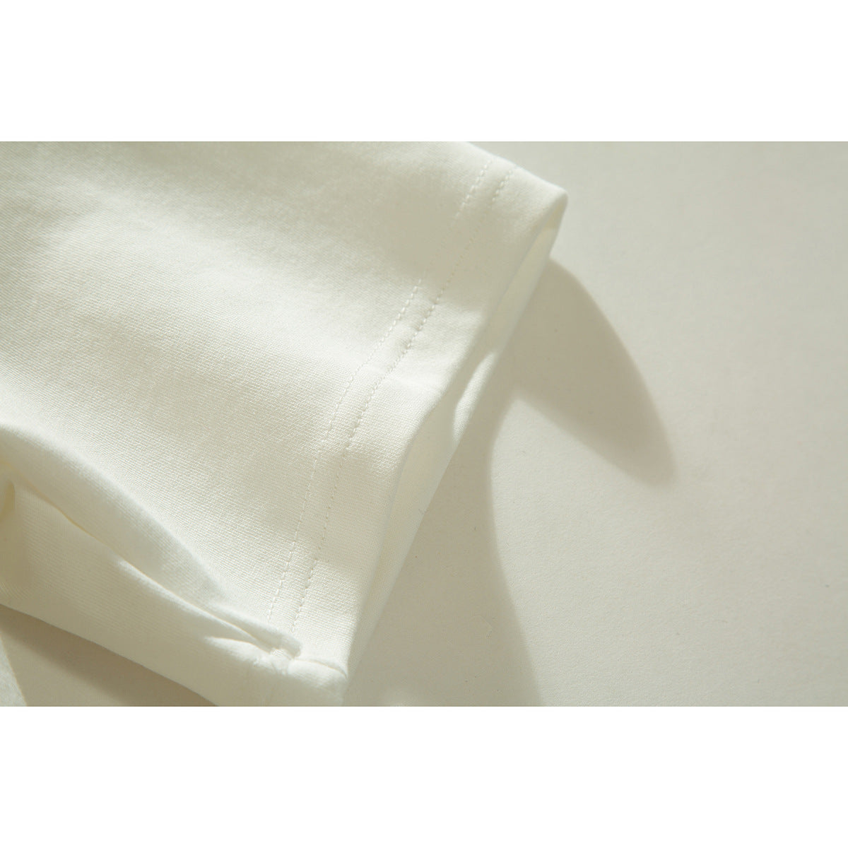 Close-up of an off-white T-shirt sleeve showing its double-stitched hem.