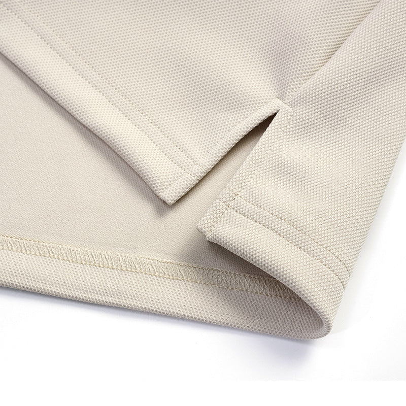 Close-up of a light beige shirt's hem and sleeve edge, showing stitching and textured fabric.