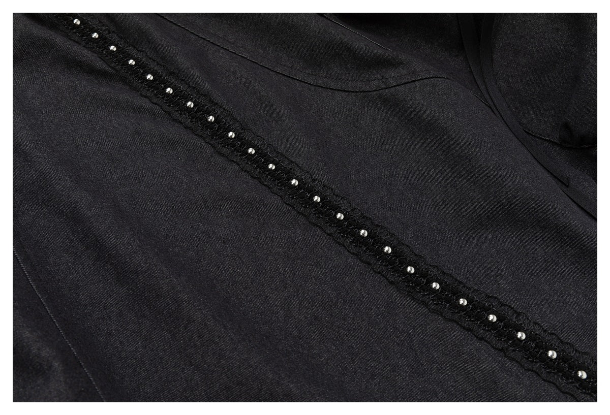 Close-up of black garment fabric with a diagonal lace-like trim lined with small silver studs.