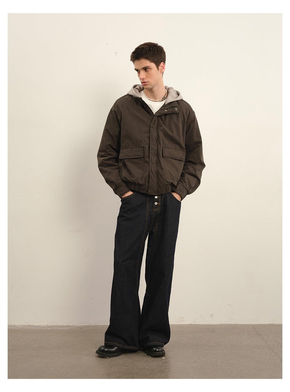 Man wearing a brown hooded jacket with flap pockets over a white tee and wide-leg dark jeans, full-length view