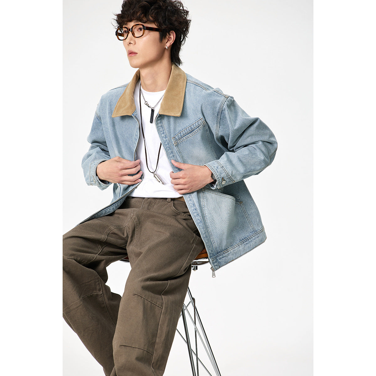 Seated model wearing a light blue denim jacket with a tan collar and front pockets.
