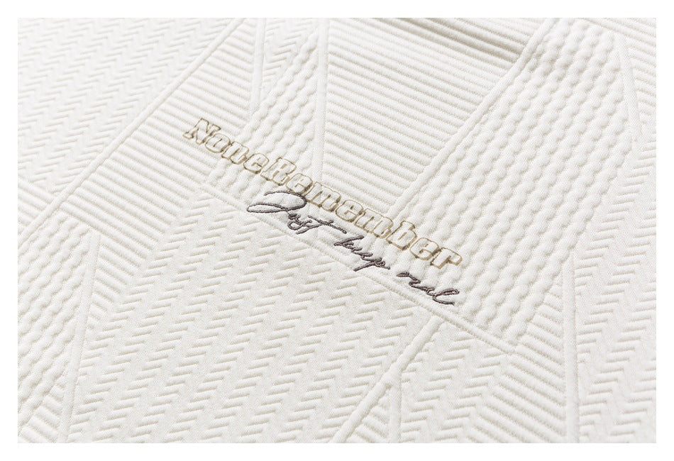 Close-up of cream quilted fabric with geometric stitched panels and embroidered English lettering.