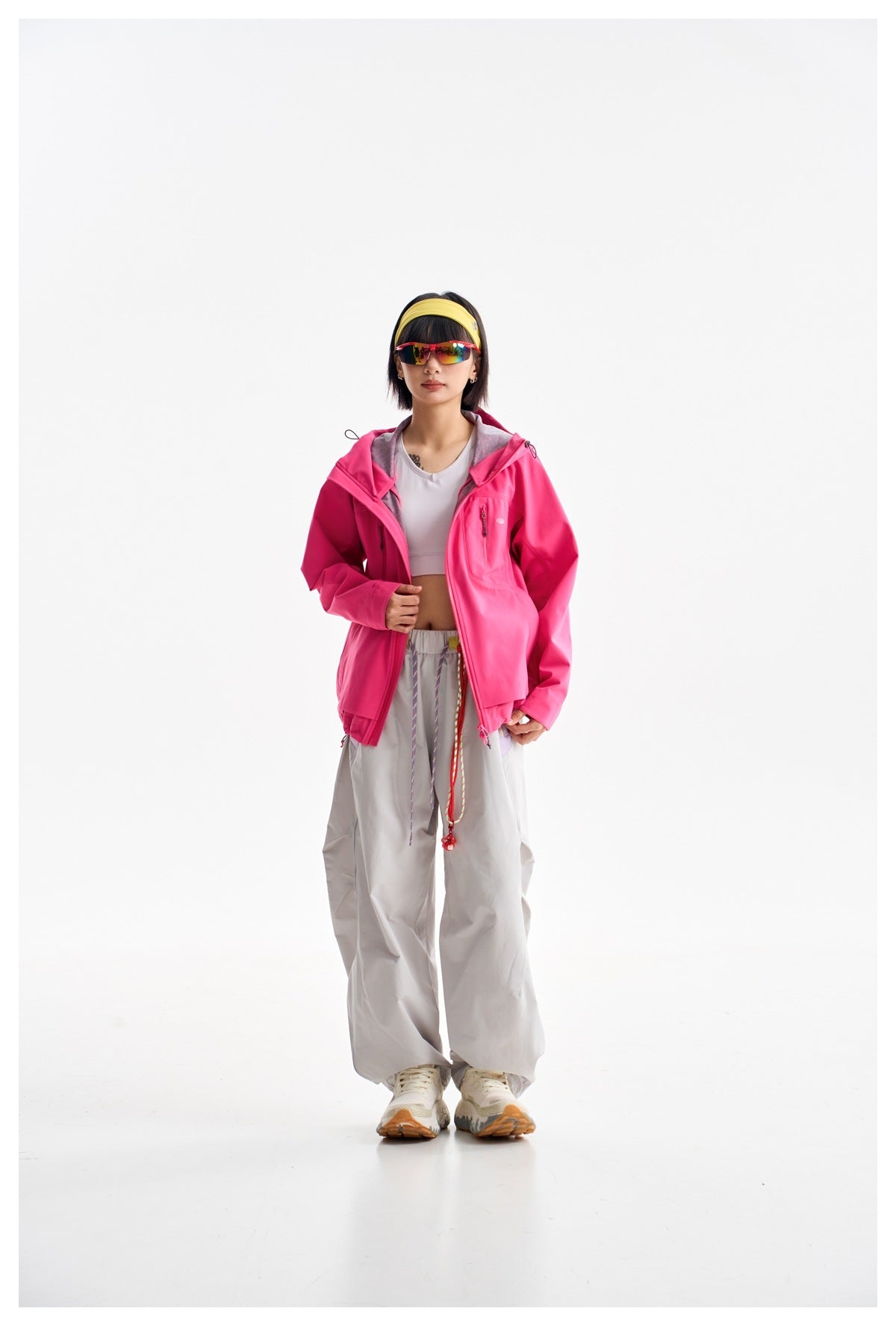 Model wearing an open bright pink hooded jacket with a chest pocket and loose light gray trousers.