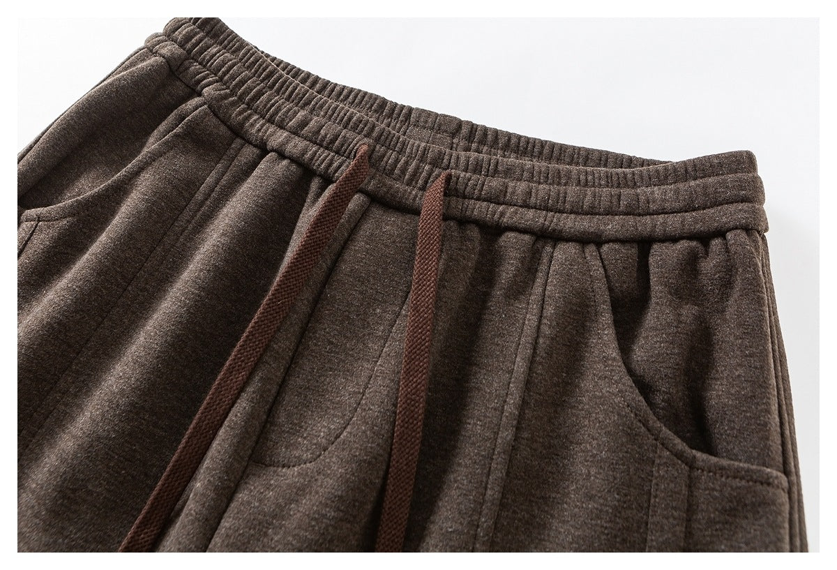 Close-up of brown trousers with an elastic waistband, dark drawstrings and curved front pockets.