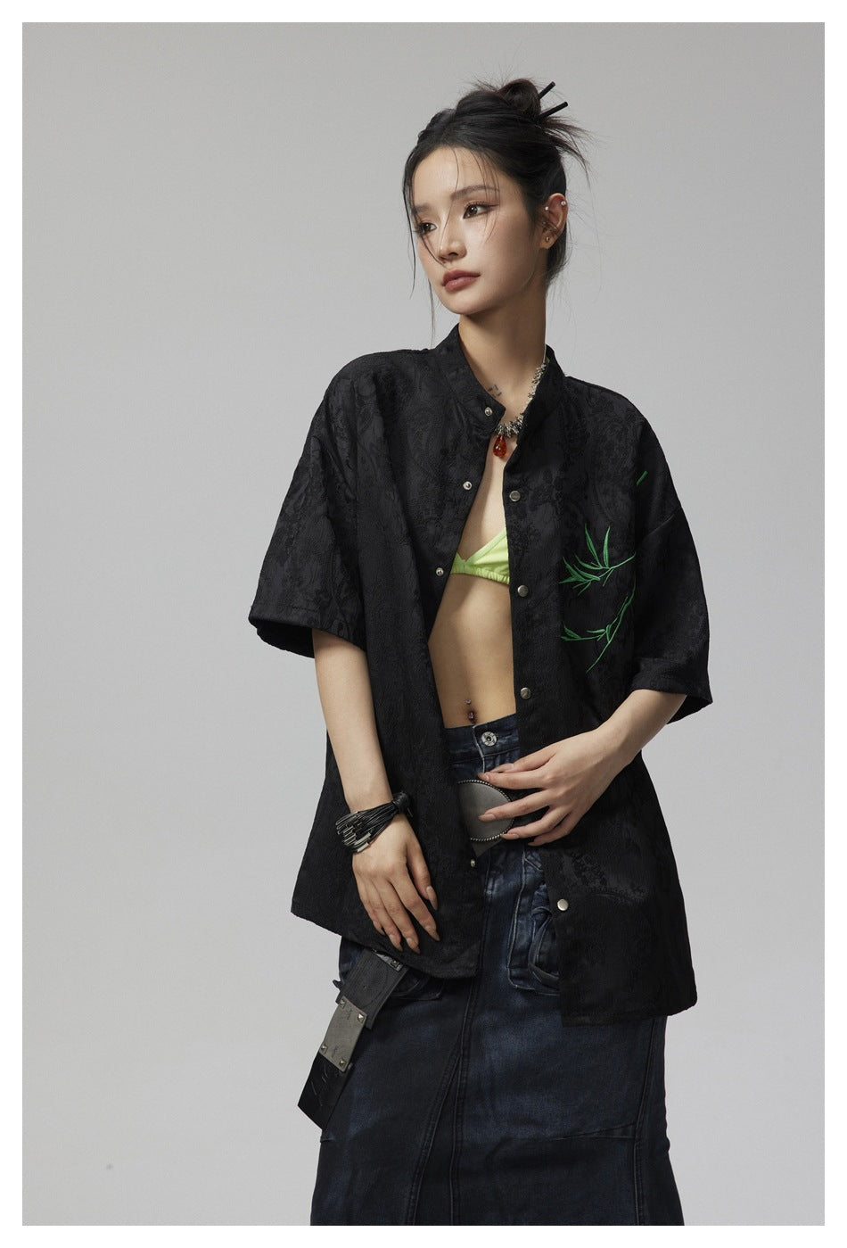 Closer view of a model wearing a black patterned short-sleeve shirt with green branch embroidery.