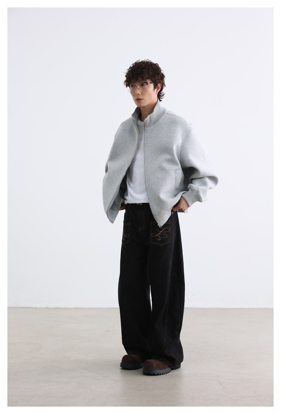Model wearing an open light gray zip jacket with a stand collar, white shirt, and loose black jeans.