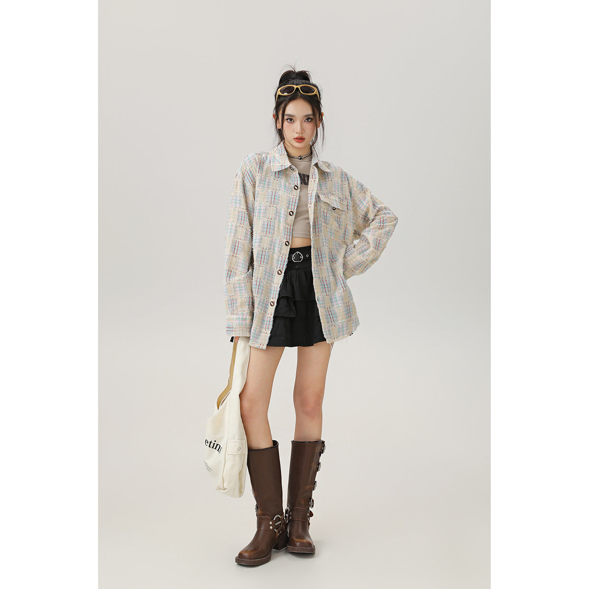 Model wearing a cream pastel-plaid oversized button-front shirt with black shorts and brown boots.