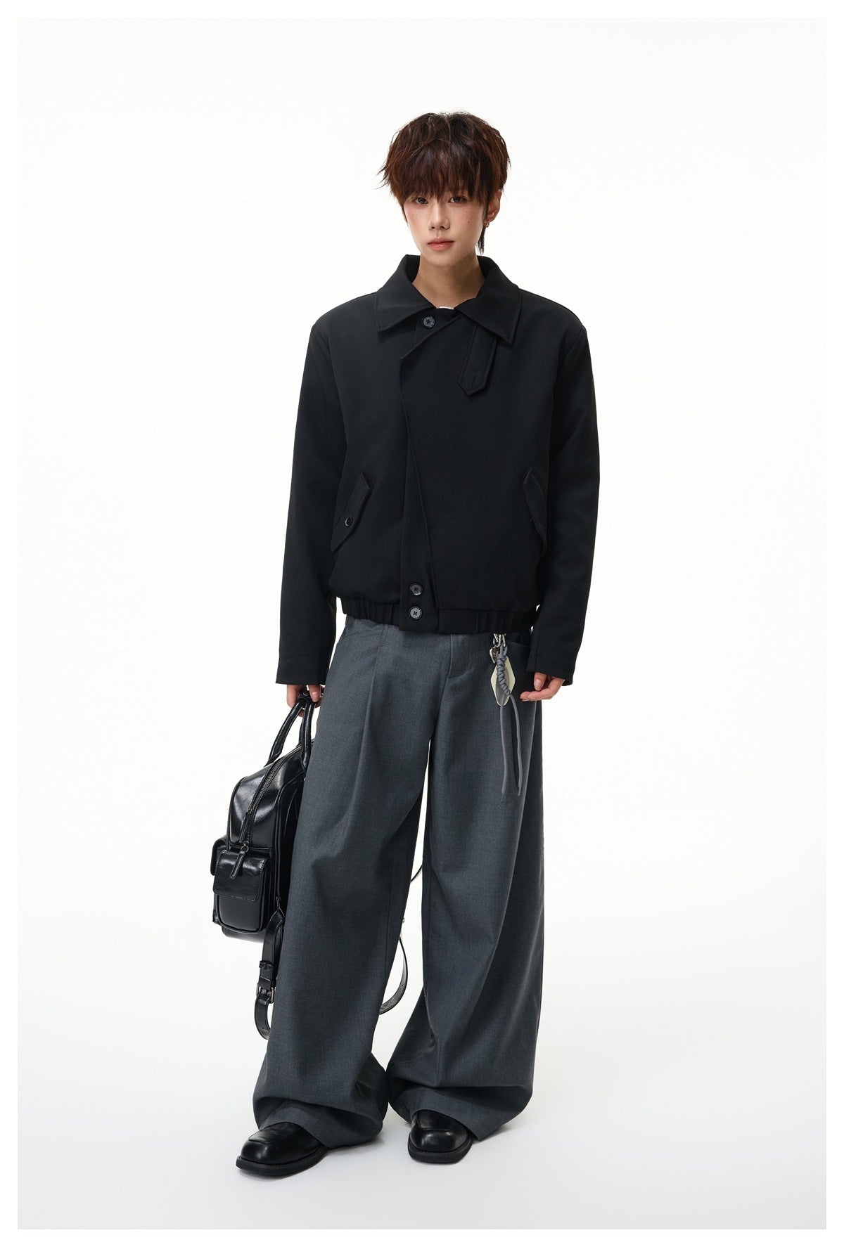 Model wearing a black cropped jacket with a wide collar and buttoned pockets, paired with charcoal wide-leg trousers.