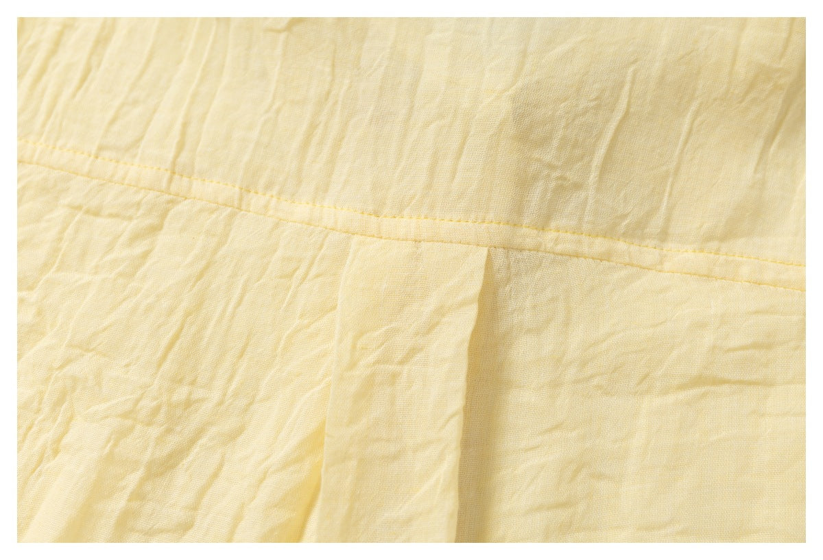 Close-up of pale yellow shirt fabric showing a horizontal stitched seam and gathered pleat.