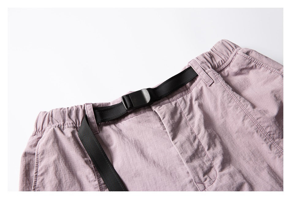 Close-up of pale mauve shorts showing the elastic waistband, belt loops, and black adjustable webbing belt buckle.