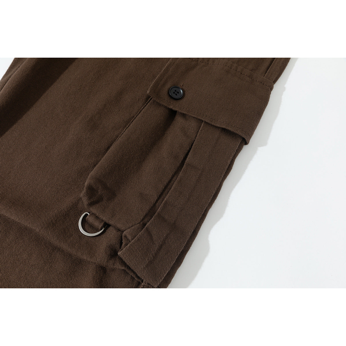 Close-up of brown cargo pants showing a buttoned flap pocket and a small metal D-ring.
