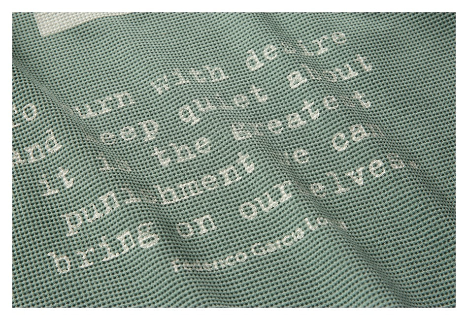 Close-up of sage-green textured fabric with scattered distressed white lettering.