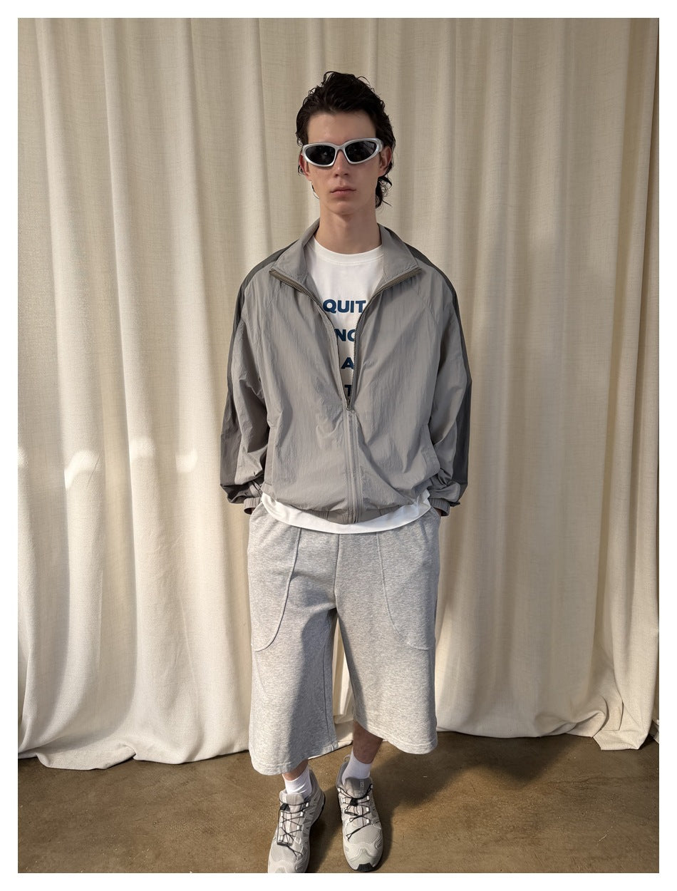 Model wearing loose light-gray knee-length shorts with curved front pockets, a gray zip jacket and white T-shirt.