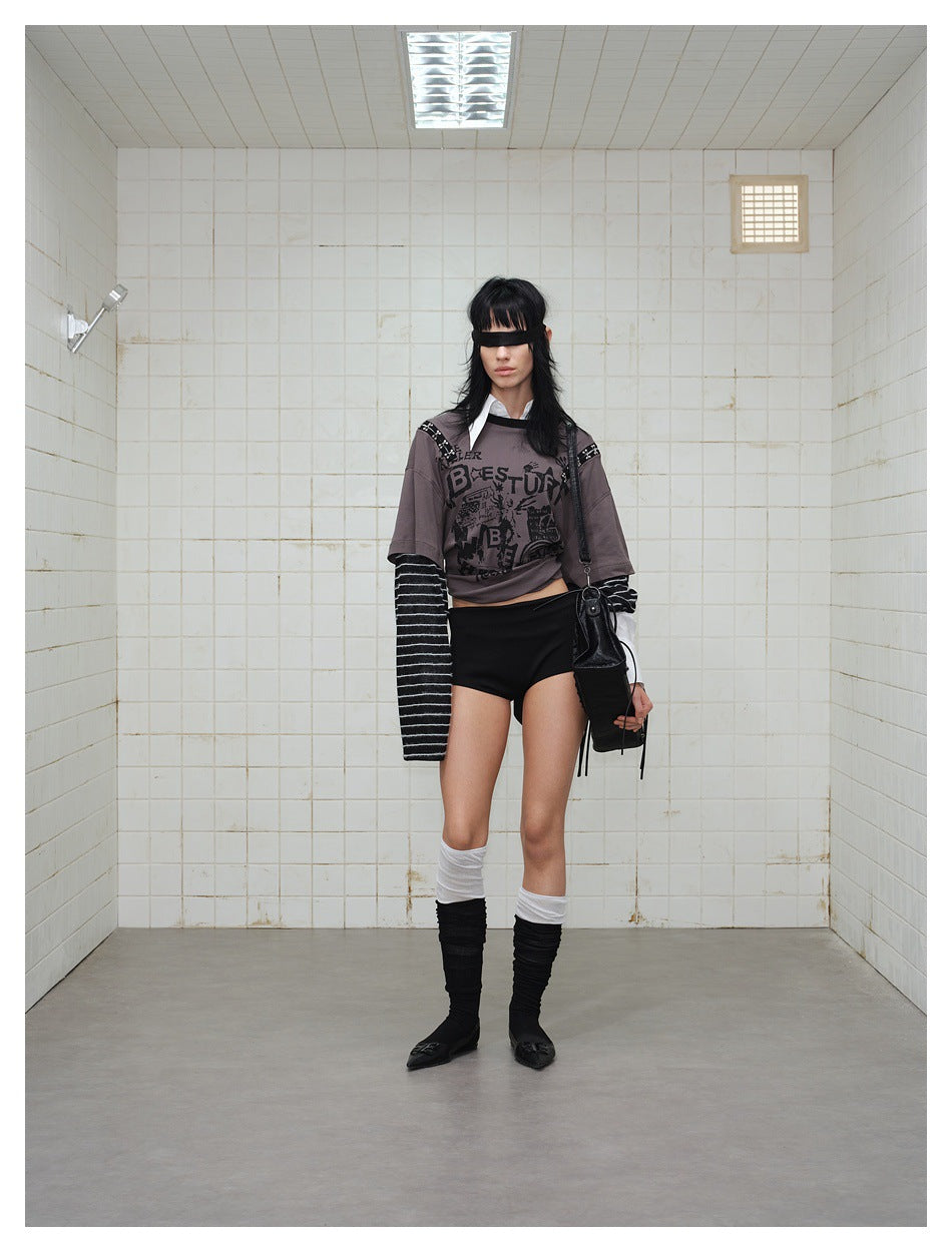 Model wearing a cropped gray graphic T-shirt over black-and-white striped sleeves, with black shorts.