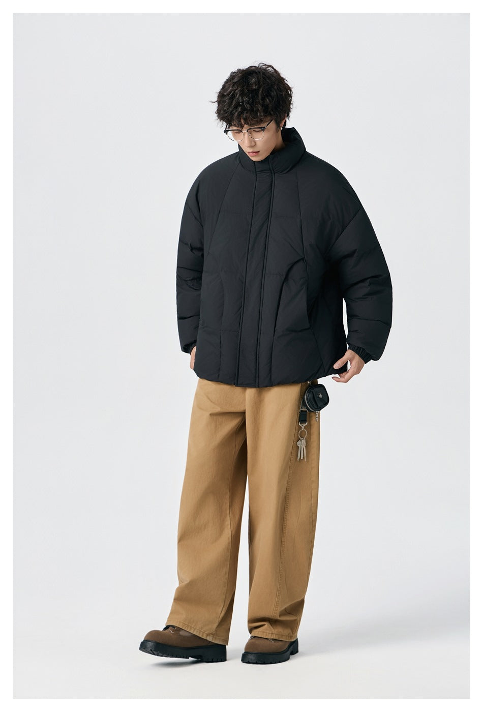 Model wearing a black high-collar puffer jacket with tan trousers, shown from the front.