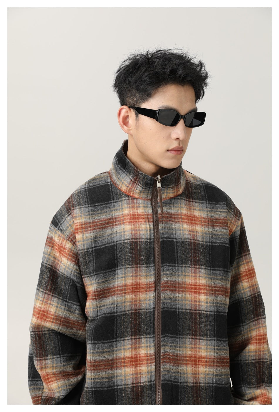 Close-up of a black, gray, and rust plaid jacket on a man, showing the stand collar and front zipper.