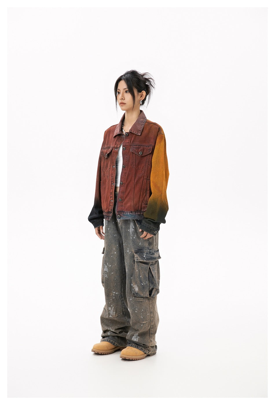 Model wearing a rust-red denim-style jacket with an orange-yellow sleeve, side view, with a white top and cargo jeans