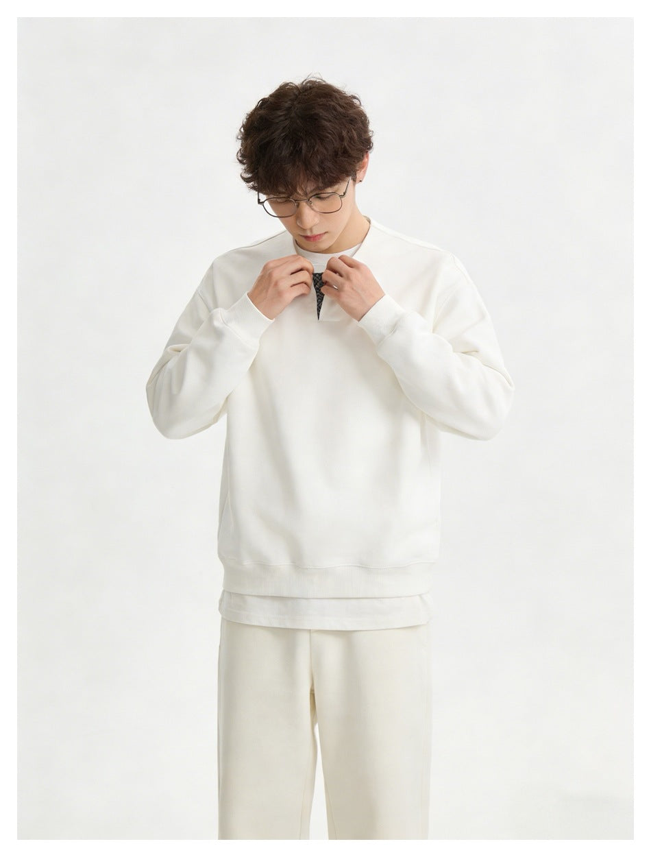 Model wearing a white crewneck sweatshirt with a small checked V-shaped neckline insert and matching trousers, adjusting the