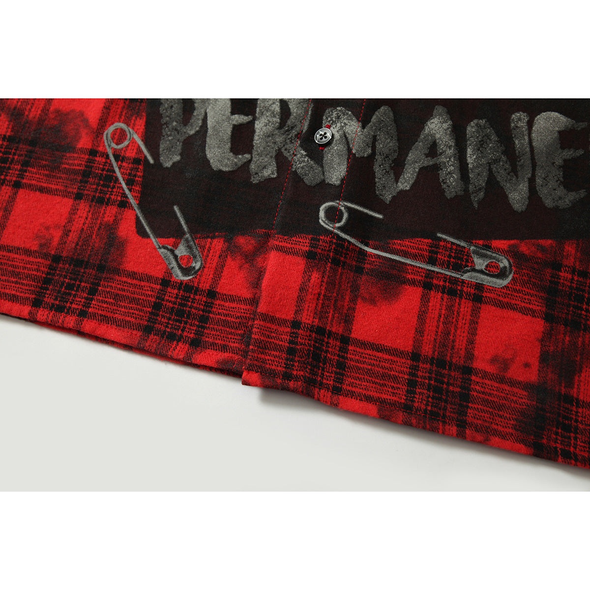 Close-up of the shirt hem and lower graphic, showing distressed lettering and safety-pin artwork on red plaid.