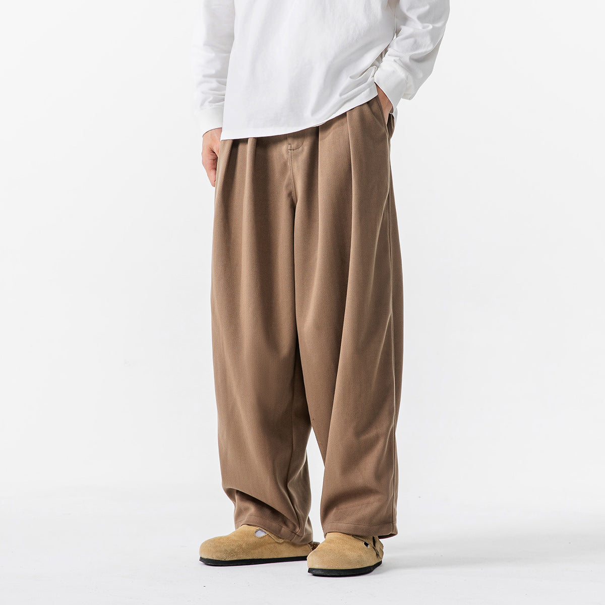 Front three-quarter view of a person wearing loose brown trousers with a white long-sleeve shirt.
