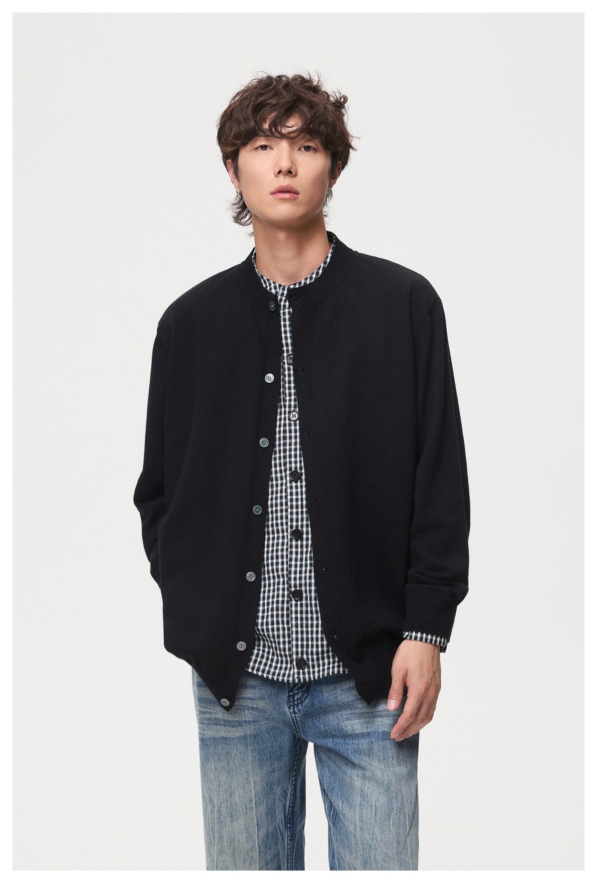 Front view of a model wearing a black button-front cardigan over a black-and-white checked shirt with blue jeans.