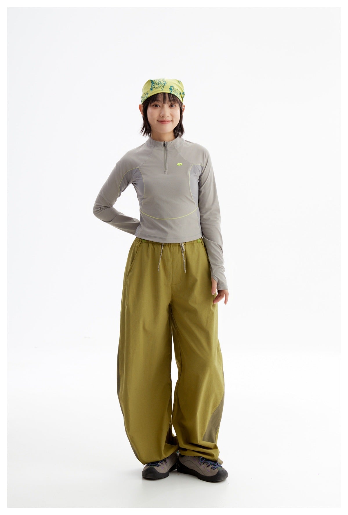 Model wearing a gray quarter-zip top with lime piping, olive wide-leg pants, and a yellow-green patterned headscarf.