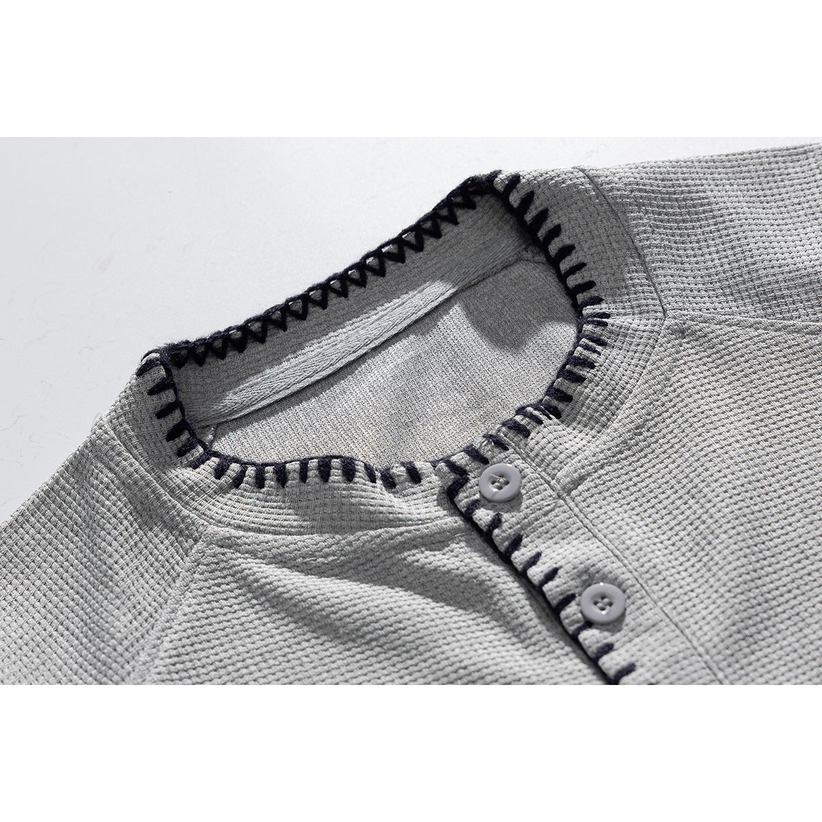 Close-up of a light gray textured shirt collar and button placket with dark contrast stitching.