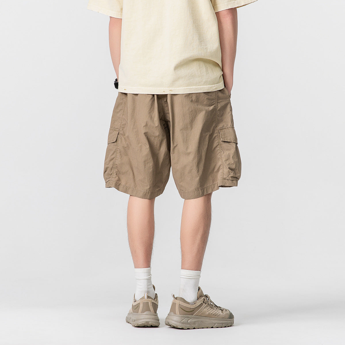 Rear view of a model wearing relaxed taupe cargo shorts with large flap pockets.