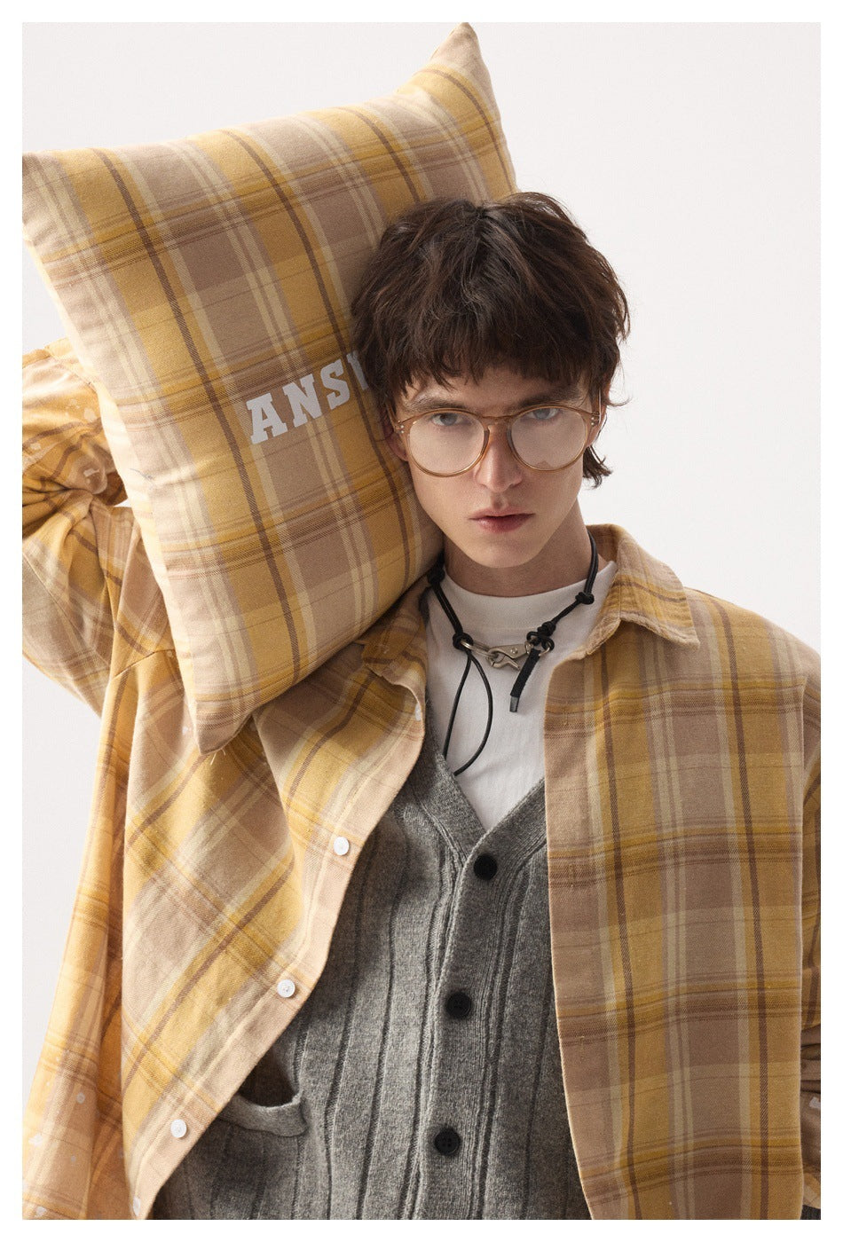 Model wearing a beige and mustard plaid overshirt over a gray buttoned cardigan and white shirt, holding a matching plaid