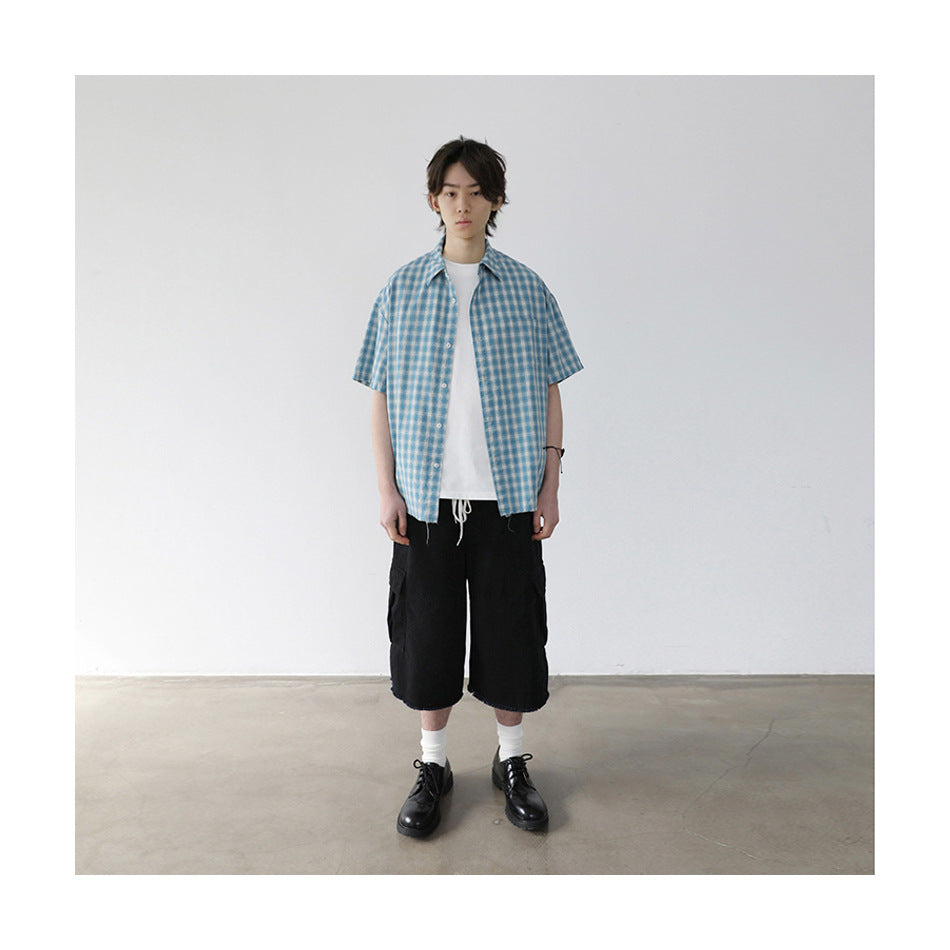 Model wearing black knee-length cargo shorts with frayed hems, a white T-shirt and a blue checked short-sleeve shirt.