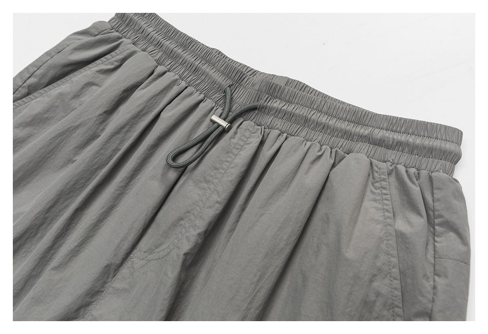 Close-up of gray shorts showing the gathered waistband, drawcord, and front pocket stitching.