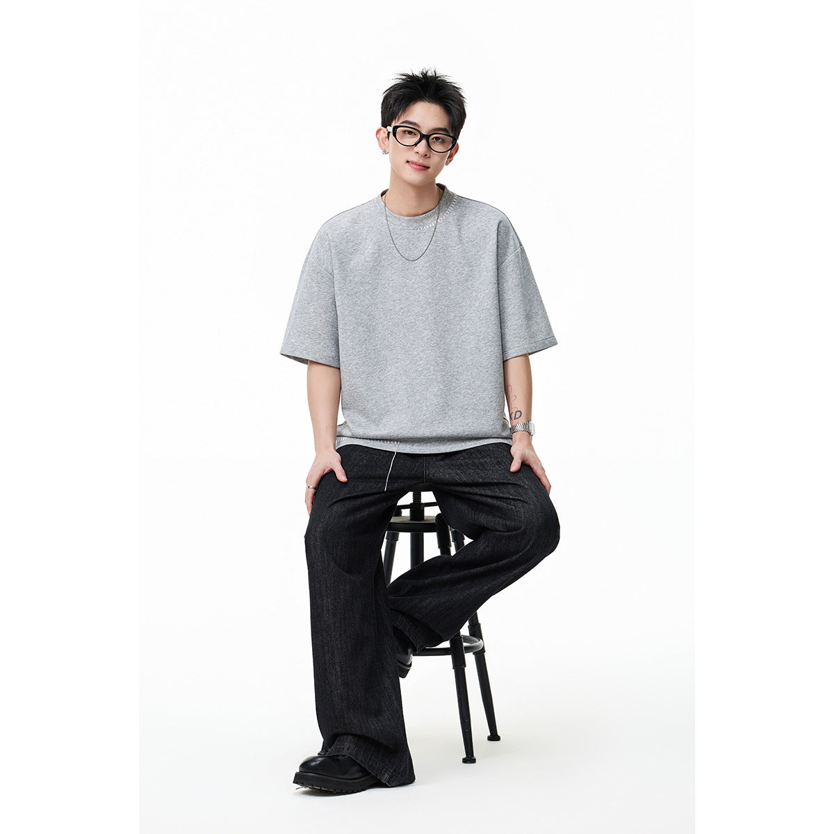 Model seated in an oversized light gray short-sleeve T-shirt with dark wide-leg pants.
