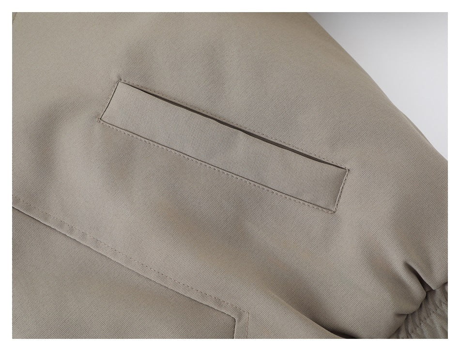 Close-up of a narrow rectangular stitched detail on the taupe jacket sleeve.