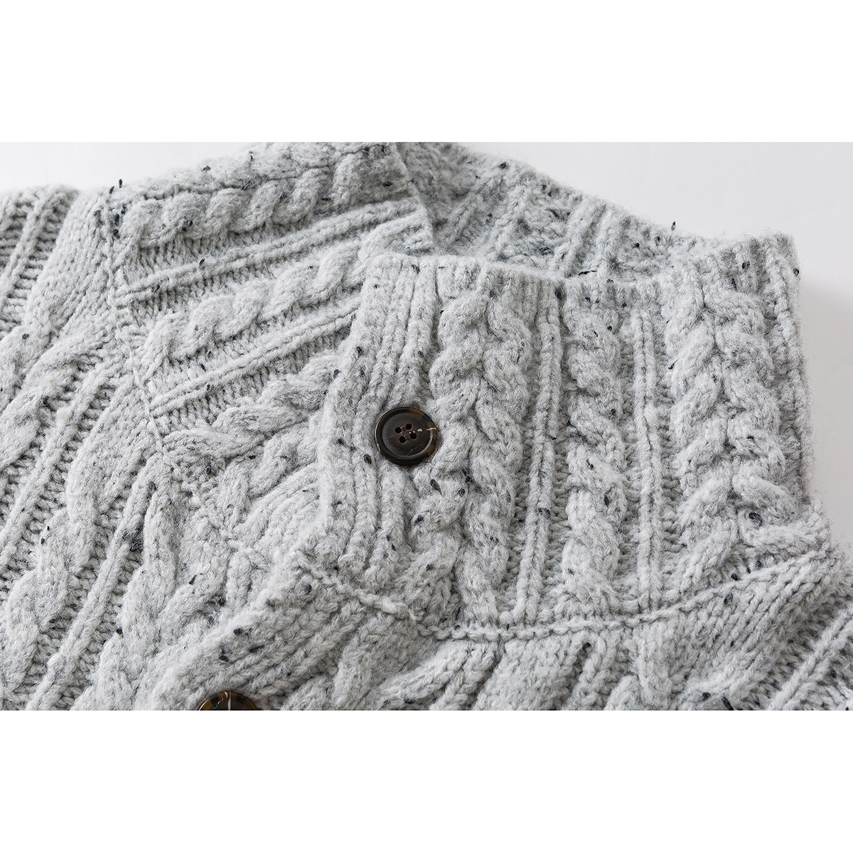 Close-up of a dark button on a light gray flecked cable-knit sweater.