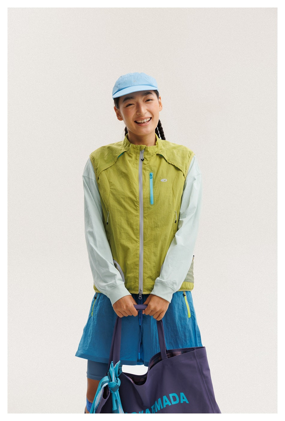 Front view of a model wearing a lime-green zip vest with turquoise pocket zips over a pale mint top.