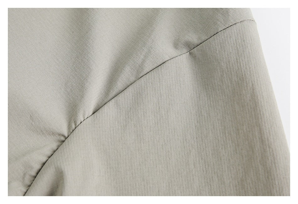 Close-up of light gray-beige fabric with a curved stitched seam and subtle fine texture.