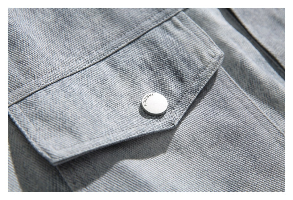 Close-up of a light gray denim jacket pocket flap with a round white button marked “FASHION.”