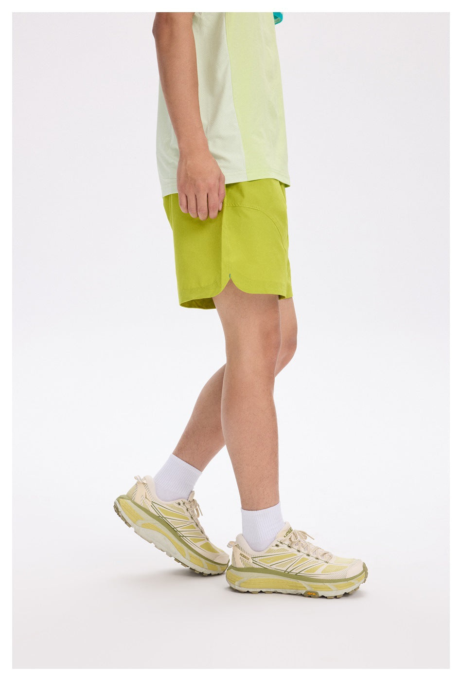 Side view of model wearing yellow-green shorts showing curved split hem, with light green top and sneakers