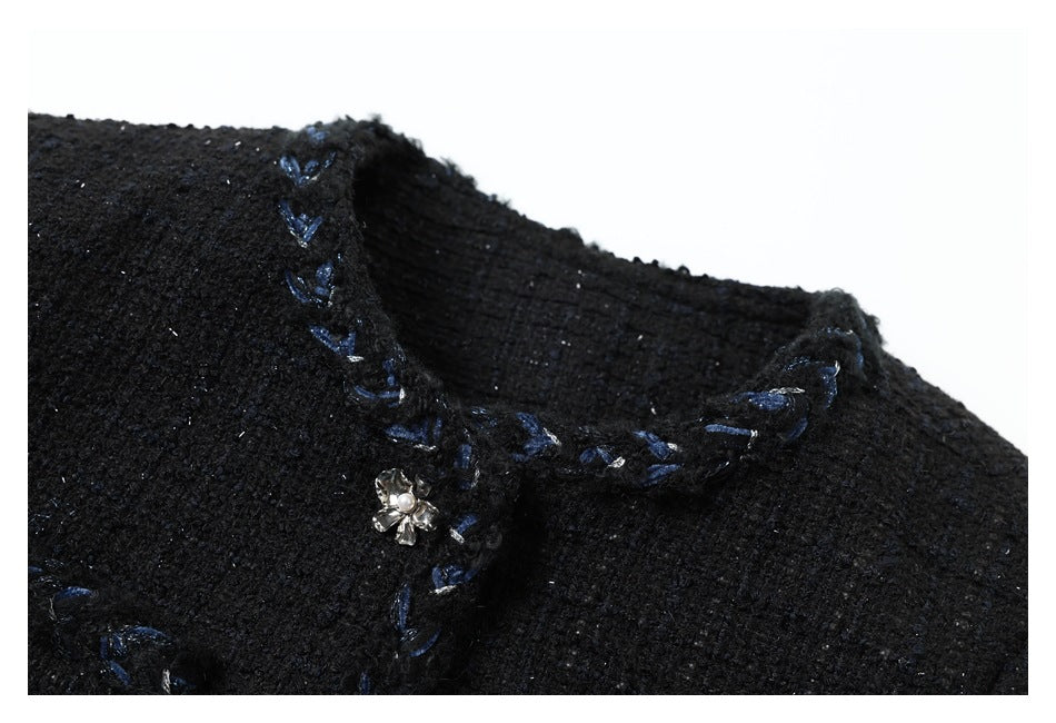 Close-up of a black jacket neckline with blue embroidered trim and a pearl-centered flower ornament.