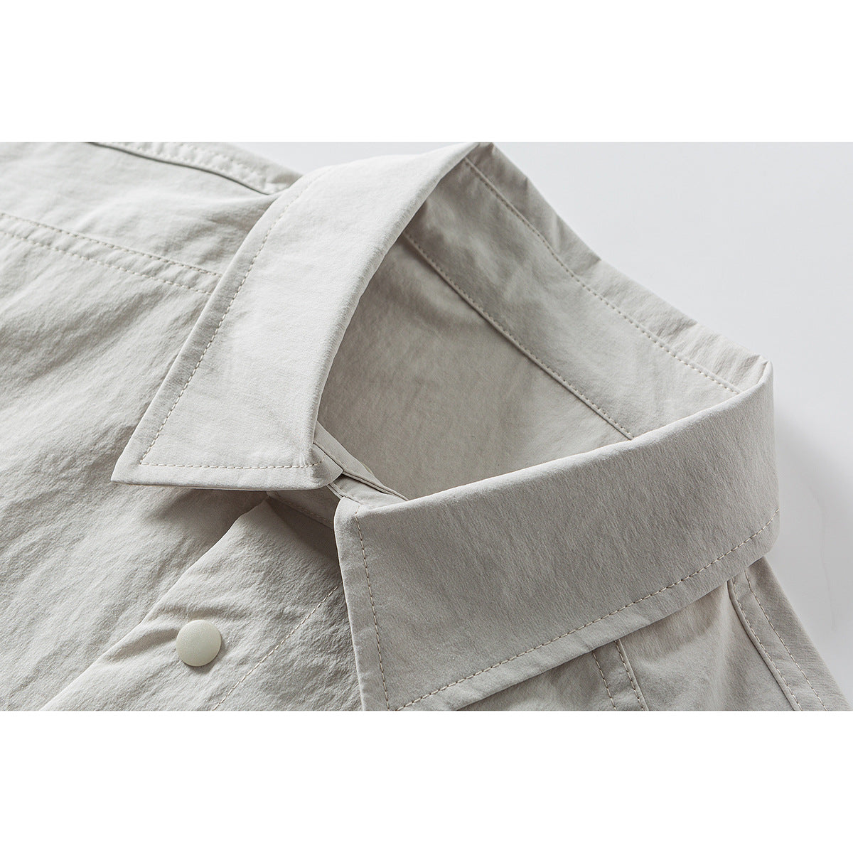 Close-up of a light beige collared overshirt showing the collar, stitching, and a pale front button.