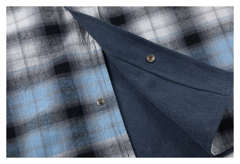 Close-up of the plaid shirt opened to show its solid navy inner panel and metal snap fasteners.